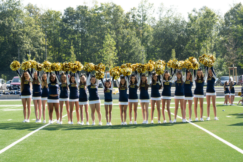 Mannschaftsfoto zum Saisonabschluss: Warum das Ende der Saison der perfekte Zeitpunkt für professionelle Teamfotos ist 2 Gruppe von Cheerleadern stehen in einer Reihe und halten ihre PomPoms über ihre Köpfe- Mannschaftsfoto Saisonabschluss
